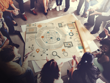 Grupo de personas reunidas en círculo alrededor de un gran diagrama estratégico sobre el suelo.