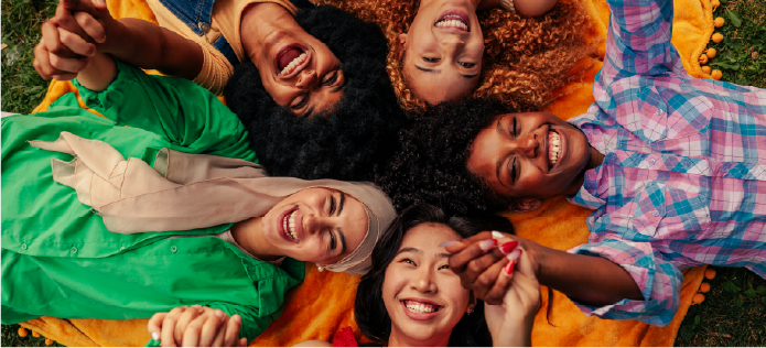 Grupo diverso de mujeres jóvenes sonriendo y tomadas de las manos, representando inclusión y diversidad cultural.